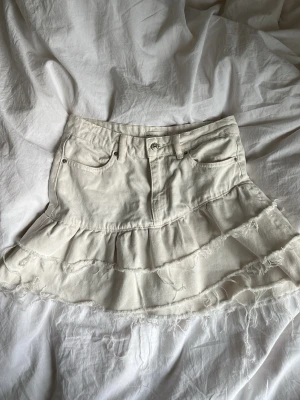 Vit volangkjol i denim - Supersöt vit kortkjol från Gina tricot i denim med volanger och råa kanter. Kjolen har klassiska jeansfickor fram och bak