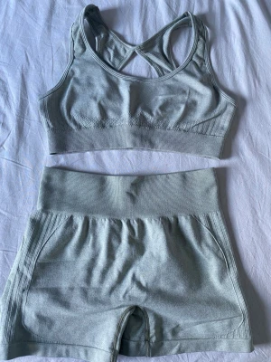 Ljusgrått sömlöst träningsset - Säljer ett ljusgrönt sömlöst träningsset med sport-bh och shorts. Bh:n har brottarrygg och bred resår under bysten. Shortsen har hög midja och scrunch-detalj bak. Materialet är stretchigt och mjukt, perfekt för träning eller chill.