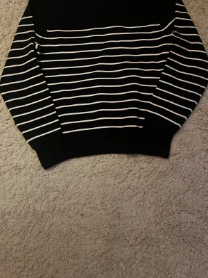 Uniqlo sweatshirt ränder - Snygg svart tröja från uniqlo med tunna vita horisontella ränder över hela plagget. Tröjan har rund halsringning och långa ärmar. Perfekt för dig som gillar en klassisk och stilren look. Endast testad