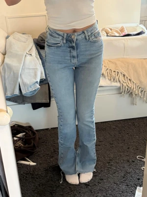 Ljusblå jeans  - Säljer ett par ljusblå jeans med bootcut-modell och hög/mid midja. Jeansen har klassiska fem fickor, dragkedja och knapp framtill. Materialet är denim med en mjuk känsla och lätt stretch. Perfekta för dig som gillar en avslappnad men trendig look.