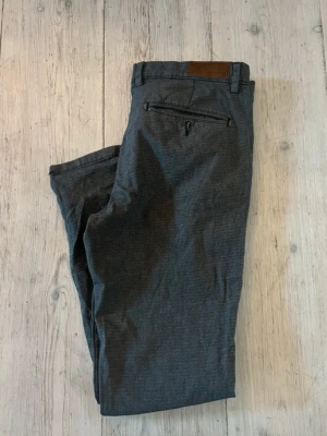 Mörkgrå chinos från Jack and Jones - Snygga mörkgrå chinos med smal passform och klassiska detaljer som bälteshällor, sidesfickor och bakficka. Modellen heter bl bl och storleken är 32/32. 