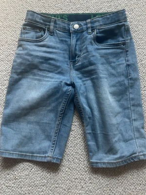 Blå jeansshorts från Levi's - Säljer ett par klassiska blå jeansshorts från Levi's med fem fickor och dragkedja. Shortsen har normal passform och är tillverkade i slitstark bomull. Perfekta för sommardagar och enkla att matcha med olika stilar.