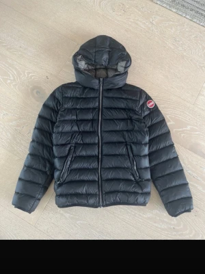 Svart dunjacka från Colmar - Snygg svart dunjacka från Colmar med huva och dragkedja framtill. Jackan har två sidofickor med dragkedja och ett Colmar-märke på ärmen. Perfekt för kalla vinterdagar och riktigt skön att bära tack vare det lätta dunmaterialet.