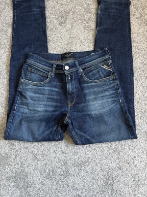 Mörkblå  jeans från Replay - Snygga mörkblå jeans från Replay med klassisk femficksmodell och slitna detaljer framtill. Jeansen har en läderpatch med Replay-logga bak i midjan och kontrastsömmar på bakfickorna. Tillverkade i stretchigt denim för skön passform. Storlek 158/14 år. Hör av er vid funderingar 🙂