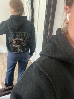 Svart hoodie med tryck och huva - Säljer en svart hoodie med stor huva och tryck både fram och bak. Trycket på ryggen har ett rymdtema med text och illustrationer. Hoodien har en klassisk passform och är gjord i mjukt material, perfekt för en chill och avslappnad stil.