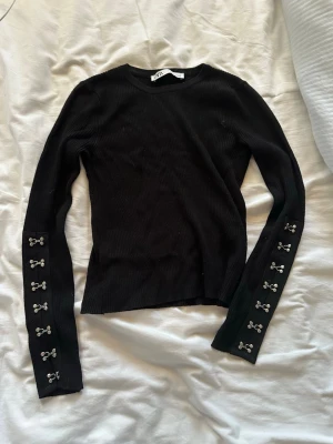 Svart ribbad tröja med detaljer - Snygg svart ribbad långärmad tröja med dekorativa silverfärgade knappar längs ärmarna. Tröjan har en tight passform och rund halsringning. Perfekt för dig som gillar stilrena plagg med en twist. as cool tröja från zara❤️
