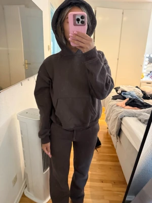 Mörkbrunt mjukisset  - Mörkbruna mjukisbyxor med rak passform och resår i midjan. Tillverkade i ett mjukt och bekvämt material som passar perfekt för chill dagar hemma. Byxorna har en enkel design utan synliga loggor eller detaljer. Hoodie storlek S och byxorna xs