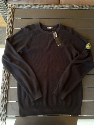 Svart stickad tröja från Stone Island - Säljer en snygg Ribbstickad tröja från Stone Island! Tröjan är i mycket bra skick förutom att den är lite solblekt på sina ställen, annars mycket fin! Om ni har några frågor så är de bara att höra av er😊