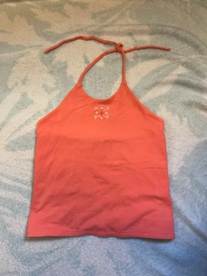 Korallfärgad halterneck linnetopp - Säljer en snygg korallfärgad linnetopp med halterneck och flätade knytband. Toppen har en liten broderad detalj framtill i vitt och är perfekt för sommaren. Tillverkad i mjuk bomull för en bekväm känsla.storlek M men passar till något som är XS eller XXS, färg koral