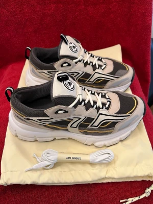 Axel Arigato Marathon R-trail Cremino, nr 42 - Säljer ett par  Axel Arigato Marathon R-trail   sneakers i beige, svart och vitt med coola detaljer och tjock sula. Skorna har snörning, meshpaneler och kontrasterande linjer i vitt och gult. Perfekta för dig som gillar streetwear och sportig stil.