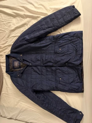 Mörkblå vindjacka från Dressmann - Snygg mörkblå vindjacka från Dressmann i quiltad design. Jackan har tryckknappar, två framfickor och en klassisk krage. Materialet är lätt och passar perfekt för blåsiga dagar. Enkel och stilren look som funkar till det mesta.                                