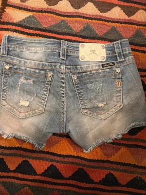 Blå slitna jeansshorts Miss Me - Säljer ett par blå jeansshorts från Miss Me med slitna detaljer och fransig kant. Shortsen har fem fickor, silverknappar och en snygg tvättad look. Dom är lågmidjade och skulle säga att storleken är 40 iEU size.