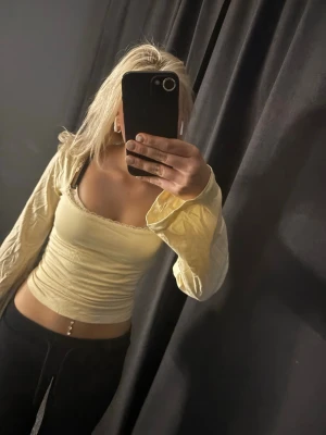 Gul croppad omlottopp med rosett - Söt ljusgul croppad omlottopp med långa ärmar och en stor rosett i ryggen. Toppen har en smickrande v-ringning och är tillverkad i ett mjukt, stretchigt material. Perfekt för dig som vill ha en trendig och bekväm topp med fina detaljer.