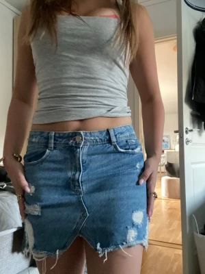 Blå jeanskjol med slitningar - Säljer en blå kort jeanskjol med slitna detaljer och sliten kant nertill. 