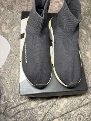  svarta sneakers - Svarta sneakers med vit logga på sidan och chunky vit sula. Stickad ovandel i stretchigt material som sitter som en strumpa runt foten. Riktigt clean och modern look som sticker ut.