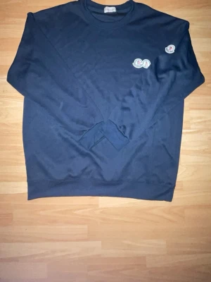 Mörkblå sweatshirt från Moncler - Mörkblå sweatshirt från Moncler med rund halsringning och logotyp-patch på bröstet samt ärmen. Tröjan har en avslappnad passform och är tillverkad i mjukt bomullsmaterial. Perfekt för en stilren och enkel look.