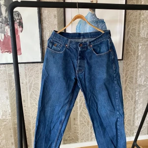 Blå jeans från Rocawear - Snygga blå jeans från Rocawear med broderade detaljer på bakfickorna. Klassisk femficksdesign och knappgylf. Perfekta för en avslappnad stil.