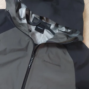 Skaljacka från peak performance medium - Vind- och vattentålig jacka från Peak Performance.  Modellen heter Pac. Grön/grå och svart. Tejpade dragkedjor. Har inte kommit till användning utan glömdes bort i garderoben så helt ny!  Herr storlek Medium. Sjukt snygg!  Väger väldigt lite så perfekt att packa ner i väskan under vandring till exempel.