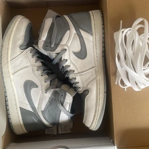 Nike Air Jordan 1 Retro High OG stealth grey - Snygga Nike Air Jordans i en stilren kombination av grått och vitt. Skorna har en klassisk hög design med snörning och rund tå. Perfekta för dig som vill ha en ikonisk sneaker med en tidlös look. Vita skosnören tillkommer.