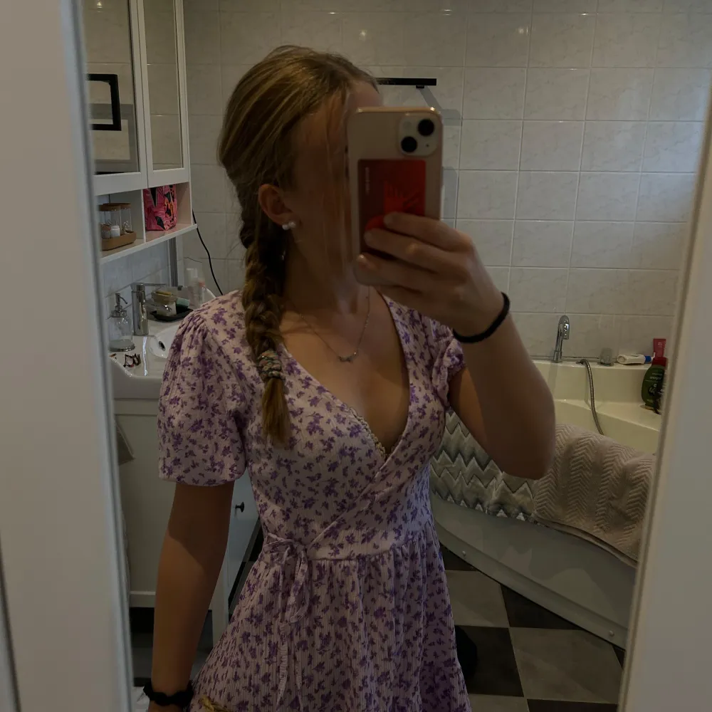 Charmig lila klänning med blommigt mönster och v-ringad design. Klänningen har korta ärmar och en omlottstil och i väldigt fint skick💜. Mekot.