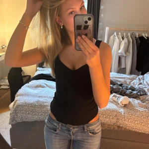 Svart ribbad body - Säljer en svart ribbad string bodysuit från Bikbok . Den har breda axelband och en djup urringning, så snygg!!