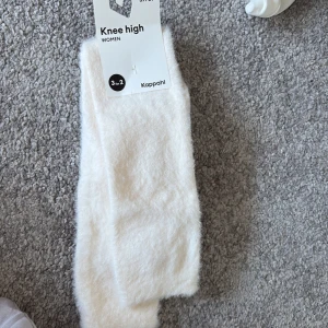 Vita knähöga strumpor från Kappahl - Säljer ett par mjuka och fluffiga vita knähöga strumpor från Kappahl. Strumporna är i storlek 37/39 och har en stilren design som passar till många olika outfits. Oöppnade. 