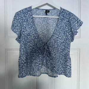 Sommartopp - Fin blå sommartopp med vita blommor, v-ringning och volangärmar. 