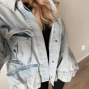 Blå jeansjacka med fickor - Säljer en blå jeansjacka med flera stora fickor framtill. Jackan har en avslappnad passform och långa ärmar. Perfekt för en casual look!