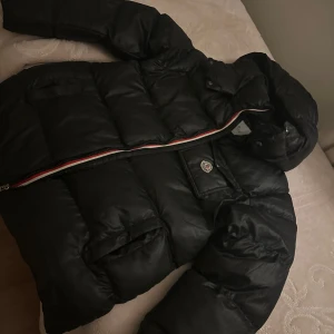 Svart pufferjacka från Moncler - Säljer en snygg svart pufferjacka från Moncler med huva och dragkedja. Jackan har en quiltad design och en liten logotyp på bröstet. Perfekt för kyliga dagar! priset  kan diskutera snabbt affär