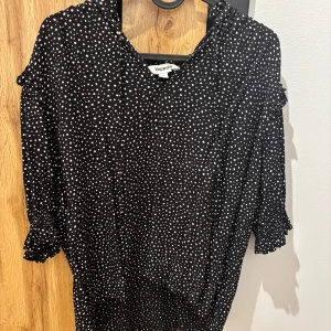 Svart prickig blus från Kappahl - Snygg svart blus från Kappahl med vita prickar och volangdetaljer vid ärmslut och hals. Blusen har trekvartsärmar och en bekväm passform. Perfekt för en stilren look!