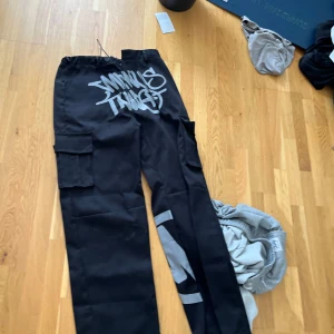 Svarta cargopants med tryck - Snygga svarta cargopants med coolt tryck i vitt. Byxorna har flera praktiska fickor och en avslappnad passform. Perfekta för en streetwear-look.