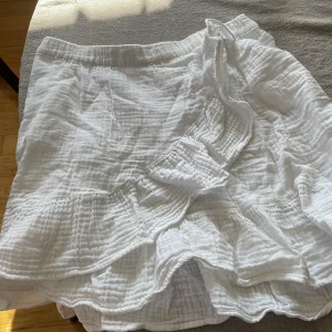 Vit kjol från Gina Tricot - Säljer en söt vit kjol från Gina Tricot med volangdetaljer. Kjolen har en elastisk midja och är perfekt för varma dagar. Den är gjord i ett lätt och luftigt material som ger en skön känsla. Jätte bra en varm sommardag!☀️🌻⛱️🍉