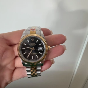 *olex klocka med tvåfärgad länk - Säljer en *olex klocka med en svart urtavla och datumvisning. Klockan har en tvåfärgad länk i silver och guld samt en räfflad guldfärgad bezel. Perfekt för den som vill ha en tidlös accessoar.