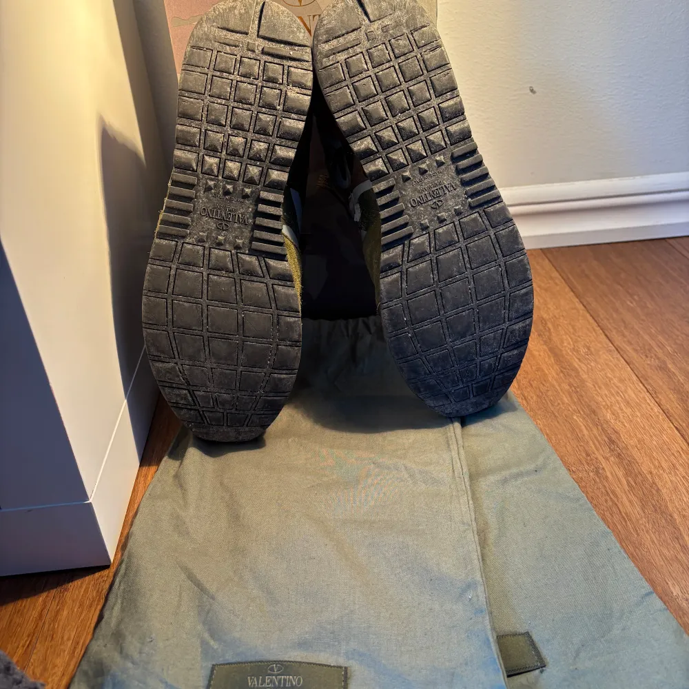 Snygga Valentino Rockrunner sneakers med ett coolt camouflagemönster i gröna och bruna toner. Skorna har en kombination av mocka och skinn, med röda detaljer på hälen. Perfekta för en stilren och trendig look.. Kengät.