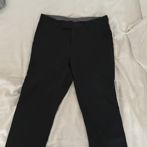 Svarta kostymbyxor från Oscar Jacobson  - Snygga svarta kostymbyxor med en klassisk passform. Perfekta för en stilren look. Byxorna har en midwaist design och är tillverkade i ett elegant material.