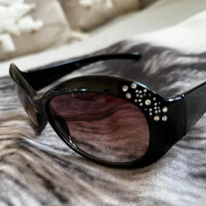 Svarta solglasögon med strassdetaljer - Snygga svarta solglasögon med stora bågar och strassdetaljer på sidorna. Perfekta för en glamorös look. De mörka glasen ger ett bra skydd mot solen.