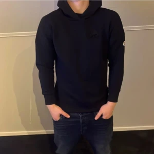 Svart hoodie från Moncler - Säljer en stilren svart hoodie från Moncler. Tröjan har en klassisk design med lång ärm och en liten logotyp på ärmen. 