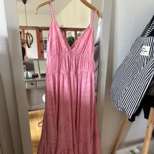 Rosa långklänning med mönster - Säljer en söt rosa långklänning med smala axelband och ett subtilt mönster. Klänningen har en v-ringad design och är perfekt för varma dagar. Den har en luftig passform och är tillverkad i ett lätt material. inga defekter🫶🏻står ingen papp men skulle säga att den passar S!
