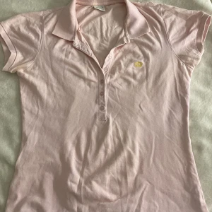 Rosa pikétröja från Gina Tricot - Säljer en söt rosa pikétröja från Gina Tricot med korta ärmar och en liten gul krona broderad på bröstet. 💕💕