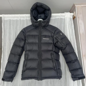 Dunjacka Peak Performance - Säljer en svart dunjacka från Peak Performance. Jackan har en praktisk huva och dragkedja framtill. Perfekt för kyliga dagar med sin långa ärm och quiltade design. En klassisk och funktionell jacka för vintern. Nyckick förutom det som syns på bild 4&5! Modell Frost down jacket, nypris 3500kr.