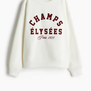 Vit sweatshirt med tryck - Säljer en vit sweatshirt med texten 'CHAMPS ÉLYSÉES Paris 1970' i rött framtill. Tröjan har en avslappnad passform och långa ärmar. Perfekt för en casual look.
