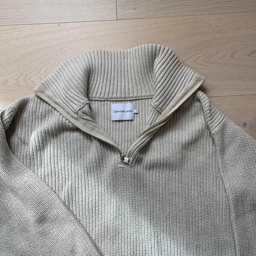 Säljer en stilren beige stickad tröja från Calvin Klein med halv dragkedja och hög krage. Tröjan har långa ärmar och ribbade muddar. Perfekt för våren. 🧥. Neuletakit & Villapaidat.