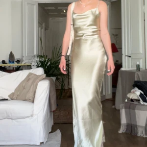 Champagnefärgad sidenklänning - Säljer min ostronfärgade balklänning i siden med smala axelband och en vacker drapering framtill. Klänningen har en öppen rygg med snörning som ger en fin detalj. Går att spänna mer i ryggen om man vill.