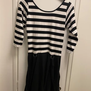 Randig klänning från Rockabella - Snygg randig klänning från Rockabella i svart och vitt. Klänningen har trekvartsärmar och en cool design med hängslen. Perfekt för en unik stil!