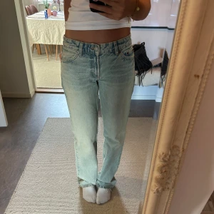 Ljusblå jeansbyxor - Säljer ett par ljusblå jeansbyxor med en klassisk femficksdesign. Byxorna har en rak passform och är perfekta för en avslappnad stil. De är low waist och har en traditionell dragkedja och knapp framtill.