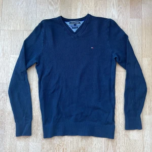 Tommy Hilfiger tröja - Säljer denna snygga tröjan från Tommy hilfiger i den trendiga färgen marinblå. Tröjan är i ett bra skick utan defekter. Perfekt att ha över en skjorta.