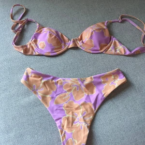 Ljus lila blommig bikini - Snygg lila bikini med stora blommor i orange och beige. Överdelen har vadderade kupor för extra stöd. Perfekt för en dag på stranden eller vid poolen.