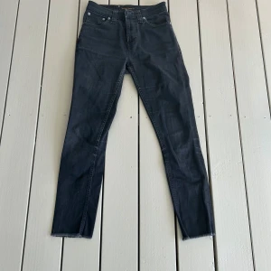Nudie jeans, pipe led i svart - Snygga svarta jeansbyxor från Nudie Jeans med en tight/slim passform. Byxorna har en klassisk femficksdesign och är tillverkade i ett stretchigt material för extra komfort. Perfekta för en stilren look. Lite rämsigt längst ner på byxorna men det kan man ta bort