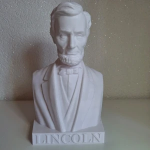 Vit byst av Lincoln - Detaljrik dekorationsfigur av Abraham Lincoln. Figuren har en snygg vit färg och har en realistisk framställning av Lincolns ansikte och klädsel. Namnet "LINCOLN" är snyggt ingraverat på sockeln. Perfekt som dekoration för hemmet eller kontoret, speciellt för den historieintresserade.  Perfekt för samlare eller som en exklusiv present.  Stilren och snygga detaljer som kommer prägla rummet den står i.   Mått ca: 24cm hög, 14cm bred & 11,5cm djup Skick: se bilder  Figuren är tillverkad av plast.  