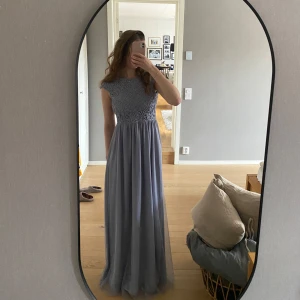 Blå balklänning med spetsdetaljer - Elegant blå balklänning med vackra spetsdetaljer på överdelen. Klänningen har en rund hals och korta ärmar. Perfekt för formella tillfällen. Säljer då jag inte använder längre, använd en gång. Str 36. Klänningen har en svag fläck på framsidan men inget som man tänker på. 